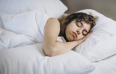 Young girl sleeping in white bed on pillows