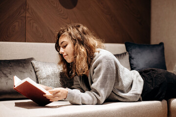 Teenager girl reading book on the couch at home