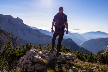 Fototapeta na wymiar Man with backpack hiking in the scenic region of the Hochschwab mountain in Styria, Austria, Europe. Mystical blue hills in the valley in Austrian Alps. Hike concept. Freedom, fresh air. Sunny summer