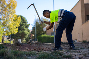 portrait of latin worker dressed in work clothes digging the earth with a sickle