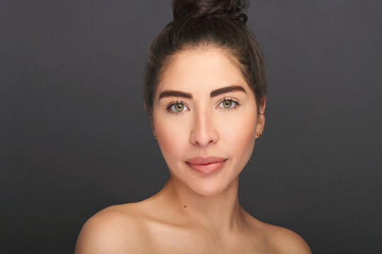 Beautiful exotic model with green eyes in beauty portrait. High fashion beauty and skin shoot in studio of latina or hispanic model with young and fresh skin. Shot on a gray background.