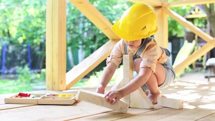 A cute European child plays with carpentry tools and wood, a child in a hard hat builds from wooden blocks. children's games,