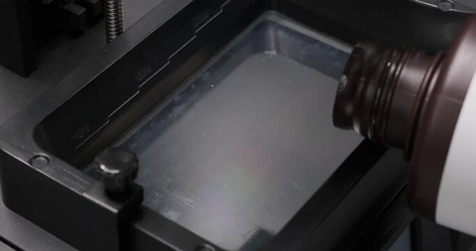 Resin SLA 3D Printer. Pouring resin into the resin vat at the begining of 3D printing. Consumer 3D printer.