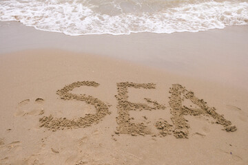 The word sea on the wet sand. Foamy waves.