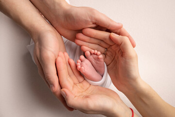 The palms of the father, the mother are holding the foot of the newborn baby. Feet of the newborn on the palms of the parents. Studio photography of a child's toes, heels and feet. Concept.