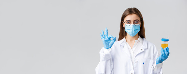 Covid-19, medical research, healthcare workers and quarantine concept. Professional doctor in scrubs, medical mask and gloves, holding patient urine sample and show okay sign, approve, making tests - obrazy, fototapety, plakaty