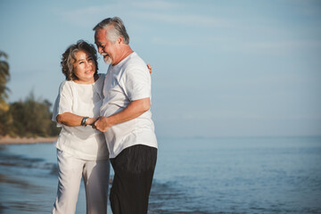 Fototapeta na wymiar The romantic Asian senior couple hugging while standing on summer beach sunset. Travel leisure and activity after retirement on vacations and summer concept. Vacation and relaxation time.