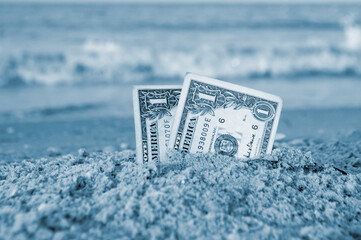 Two one dollar bills half buried in sand on sandy seashore close-up. Concept money, finance,...