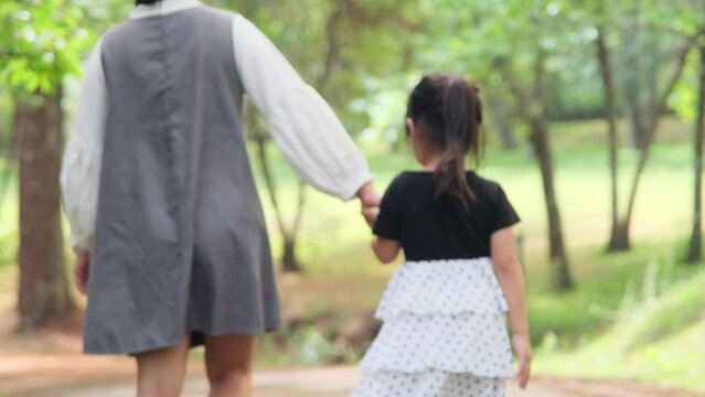 Mother holding daughter's hand in the outdoor spring garden and walking together. family relationship concept