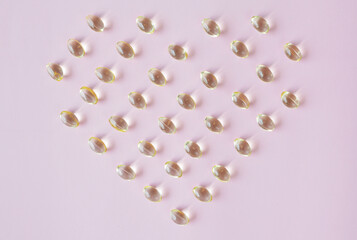 Vitamin E capsules in heart shape on pastel pink background
