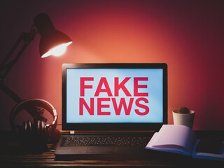 Laptop, headphones, table lamp, notebook, phone and flower at workplace. Distance work concept in quarantine. Modern freelance. Fake news inscription on laptop screen. Information war concept.