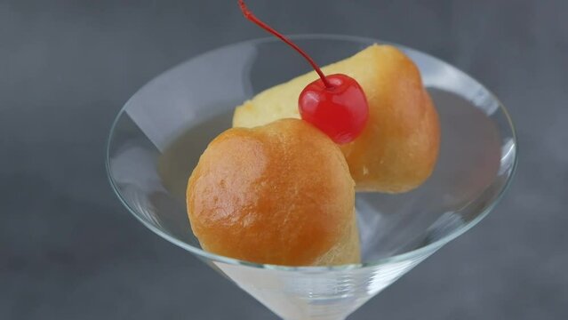 Neapolitan Rum baba (or baba au rum) in a martini glass with a cocktail cherry on a black background. Small yeast cakes soaked in rum syrup. Traditional Italian pastry. Rotation, selective focus.