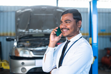 Supervisor or manager busy talking on mobile phone at garage about car repair or maintenance...