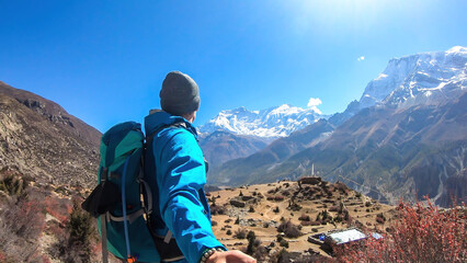 A man hiking and taking a selfie with snow caped Annapurna chain in the back, Annapurna Circuit Trek, Himalayas, Nepal. High mountains around. The man is admiring the landscape. Serenity and calmness.