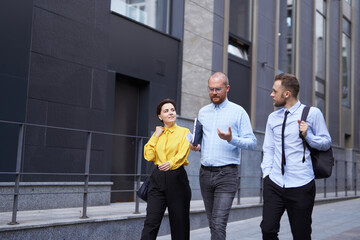Business people outdoors. Three white collar workers in formal wear walking along the street during the break at office, urban background. Brainstorming or discussing project. High quality photo