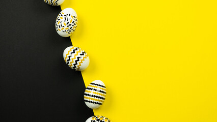 Golden, black, white eggs with a geometric pattern on a yellow and black background. View from above. Easter card with copy space for text. Web-banner