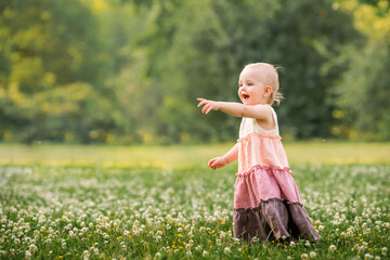 A little blue-eyed girl walks in a meadow with white clover in summer in a long vintage linen...