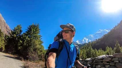 Cercles muraux Manaslu A man taking a selfie while trekking along Annapurna Circuit in Nepal. He is enjoying the view and trek. There is a lush green Himalayan valley around him. Snow caped mountains in the back