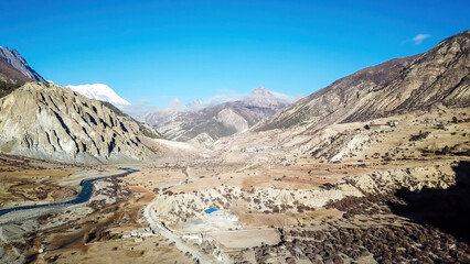 Way to Upper Pisang, Annapurna Circuit Trek, Nepal. Clear sky above the peak. Picturesque landscape, river in the bottom on the valley, small trees on the shores. White Himalayas mountain peaks