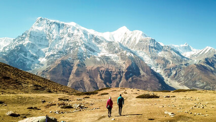 Een paar dat op de Annapurna Circuit Trek loopt, Himalaya, Nepal. Annapurna-ketting met sneeuwkap aan de achterkant. Helder weer, droog gras, besneeuwde toppen. Grote hoogte, enorme bergen. Vrijheid en avontuur