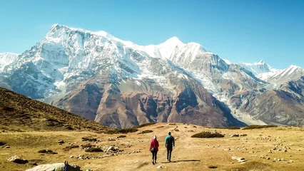 Fotobehang Annapurna Een paar dat op de Annapurna Circuit Trek loopt, Himalaya, Nepal. Annapurna-ketting met sneeuwkap aan de achterkant. Helder weer, droog gras, besneeuwde toppen. Grote hoogte, enorme bergen. Vrijheid en avontuur