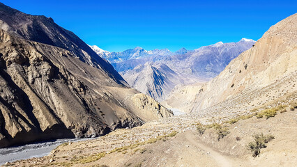 A view on a dry bottom of Himalayan valley. The valley is located in Mustang region, Annapurna Circuit Trek in Nepal. In the back there is snow capped Dhaulagiri I. Barren and steep slopes