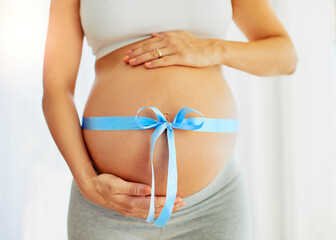 My little prince is on the way. Cropped shot of a pregnant woman with a blue ribbon tied around her belly.