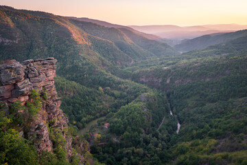 Obraz premium Golden hour view of a river canyon with hills covered by forests lighten by golden light and impressive vertical cliff in the foreground 1