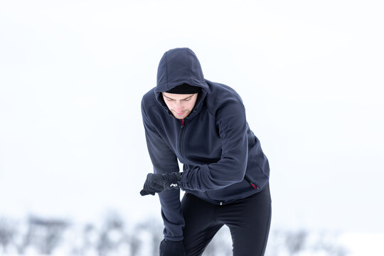 kurze Verschnaufpause - junger Jogger checkt die Zeit auf seiner Fitnessuhr w&auml;hrend einer Laufeinheit im Winter