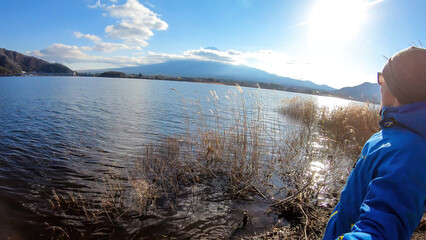 Fototapeta na wymiar A man walking at the side of Kawaguchiko Lake, Japan with the view on Mt Fuji, while taking a selfie. The magnificent mountain surrounded by clouds. Serenity and calmness. Exploring new places.