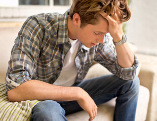 Obraz premium This headache is killing me. A young man sitting on a couch with his hand in his hair as if in pain.