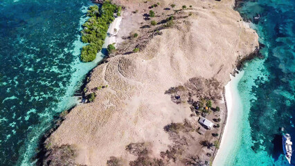 A top down drone shot of paradise island in Komodo National Park, Flores, Indonesia. The island has scarcely any trees and bushes and is surrounded with idyllic white sand beaches. Island hoping