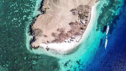 Top down drone shot of paradise island in Komodo National Park, Flores, Indonesia. The island has scarcely any plants and is surrounded with idyllic white sand beaches. Few boats anchored on the shore