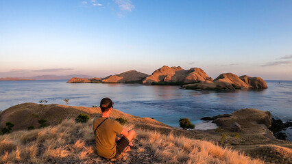 A man standing on top of a small island, facing a rising sun over Komodo National Park, Flores,...