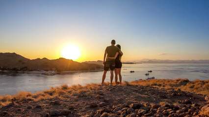 A couple standing and hugging on top of a small island, enjoying the morning sun over Komodo National Park, Flores, Indonesia. Golden hour over the islands and sea. They are enjoying their time. Love