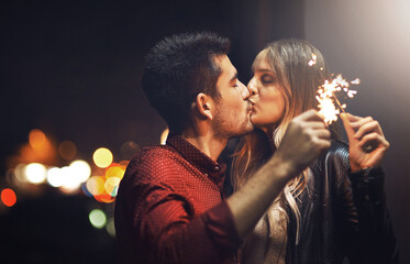 The sparks fly when we kiss. Shot of a happy young couple celebrating with sparklers outside at night.