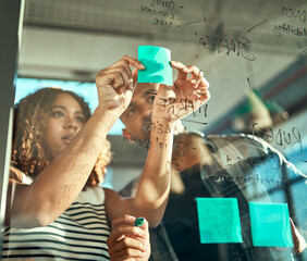 It may be small, but itll definitely be successful. Shot of two focussed young work colleagues putting up sticky notes on a glass wall while brainstorming together in the office at work. - obrazy, fototapety, plakaty