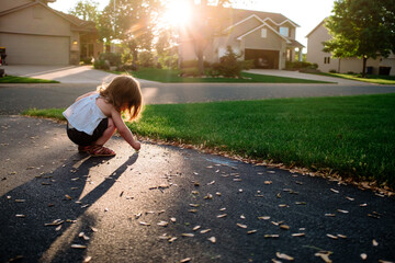 A toddler plays with leaves in a driveway at sunset