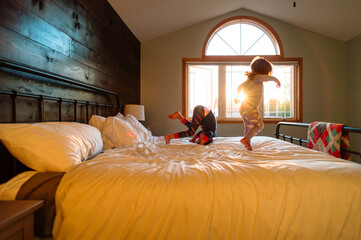 Two children in pajamas jump on a bed at sunset