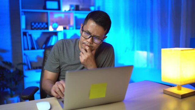 freelance man working on laptop At home at night. Man freelancing, thinking, serious while working at home at night. Freelance work and work from home concept.