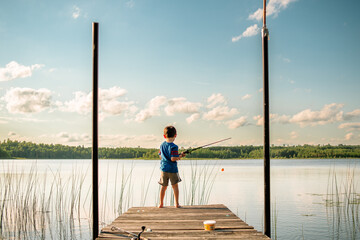 A young boy in a life jacket holds a fishing pole at the end of a dock in northern Minnesota - Powered by Adobe