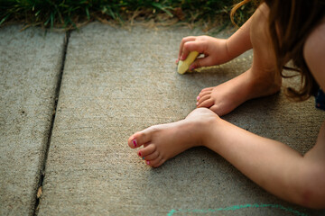 A barefoot child plays with yellow chalk on a concrete sidewalk