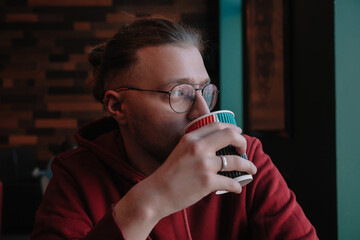 Portrait of happy male freelancer in optical eyewear for vision correction smiling at camera during break from web working online, cheerful hipster blogger sitting in cafe with mockup laptop