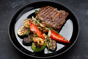 Meat steak with grilled vegetables on a black plate