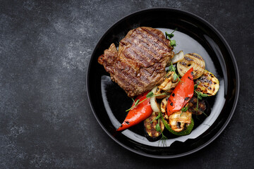 Meat steak with grilled vegetables on a black plate