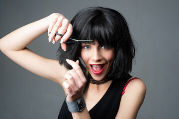 Funny young girl with short brunette hair and hairdressers scissors. Attractive young woman is...