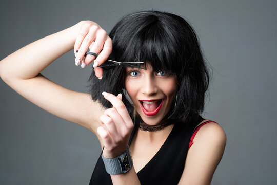 Funny young girl with short brunette hair and hairdressers scissors. Attractive young woman is cutting hair.