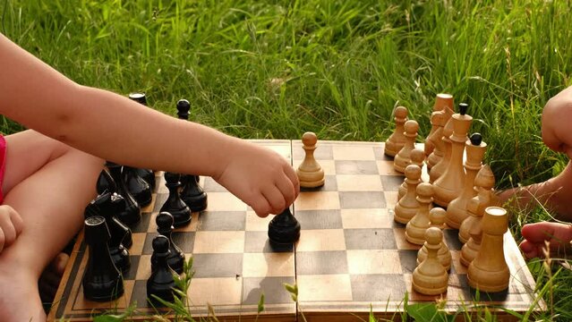Close-up of the first move in chess by a pawn on an old worn-out chessboard. Children play chess outdoors in the fresh air in the garden, sitting on the lawn. 