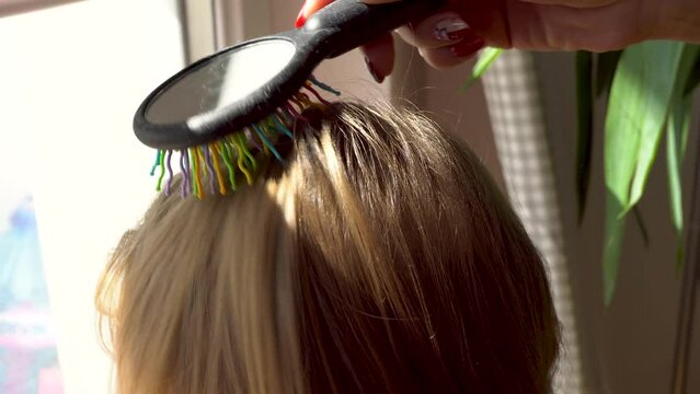 Back view of a mother combing her daughters hair. Close up video with shallow depth of field. Concept of hair care, hair brushing and beauty. 