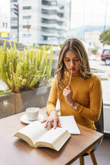 beautiful young latin woman with long blonde hair sitting concentrated on a book with a pencil to...